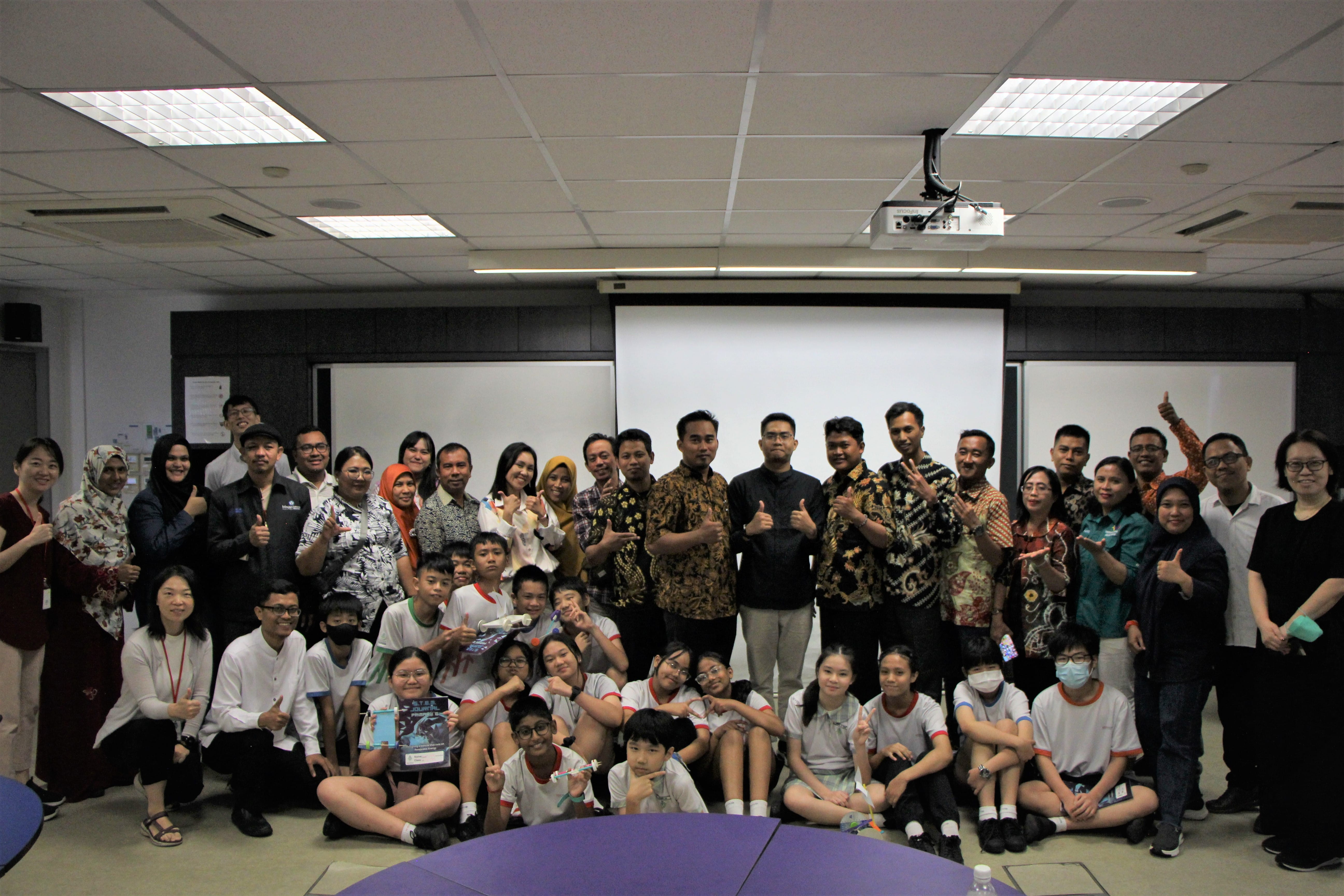 A large group of adults and students posing together in a classroom with a projector screen behind them.